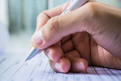 Close up of hand filling out paper survey form with pen